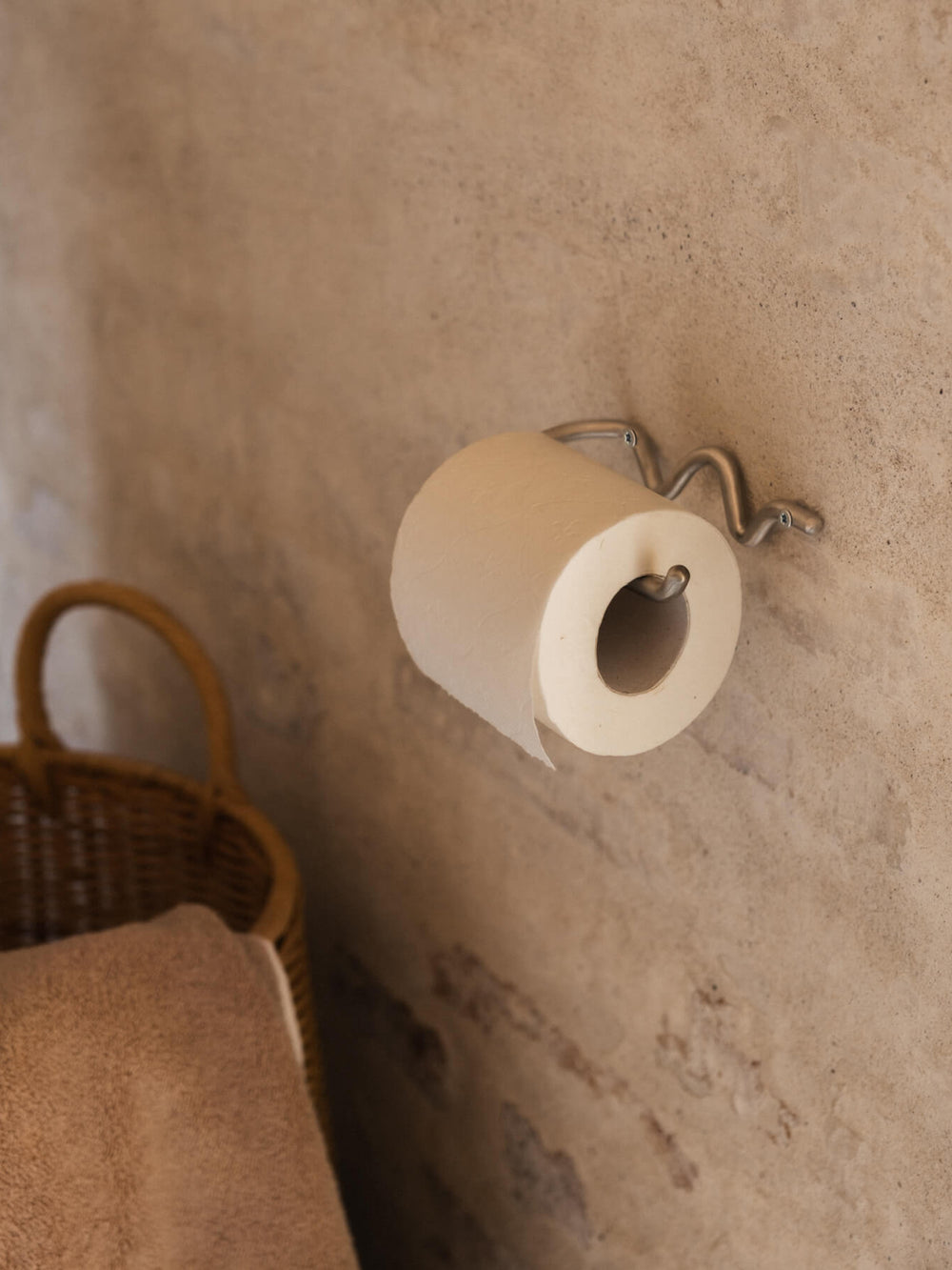 Portarrollos curvo montado en una pared de yeso, con una cesta trenzada y una toalla al lado