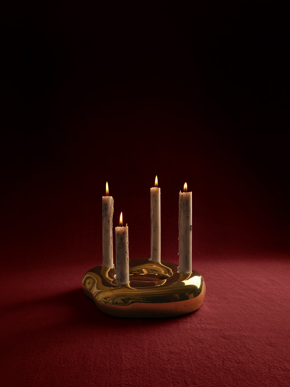 Cuatro velas encendidas en un candelabro circular redondeado sobre un fondo rojo intenso