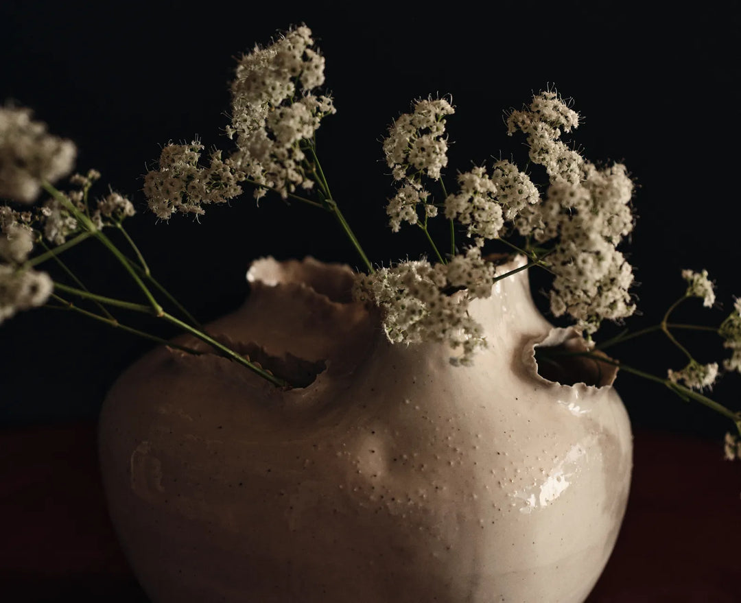 Collection d'accessoires, gros plan d'un vase blanc cassé aux ouvertures déchirées avec des fleurs blanches